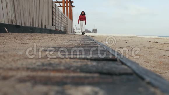 一个穿红色衬衫的女孩走在沙滩上的木地板上视频的预览图