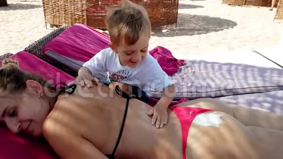 4k视频小男孩在沙滩上躺在日光浴床上涂防晒霜视频的预览图