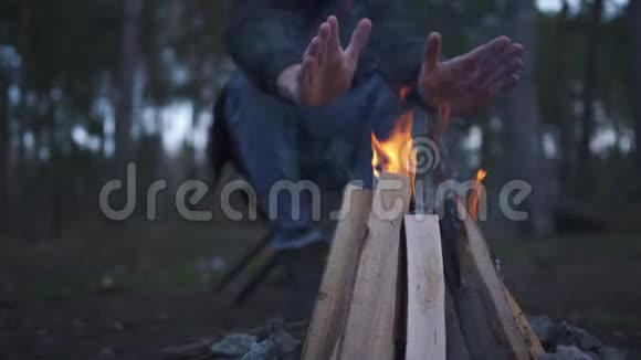 一个人坐在椅子上搓着双手取暖无胡子的人在森林里的炉火旁休息视频的预览图