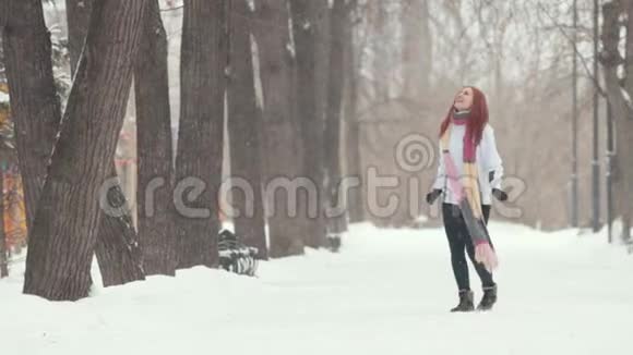 冬季公园一场大雪站在人行道上的一个红头发的女人用嘴巴捕捉雪花视频的预览图