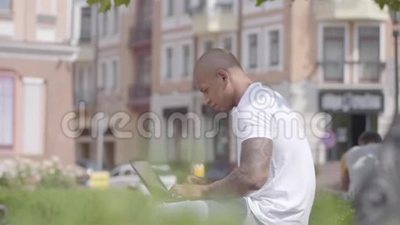 英俊的秃顶的中东男人拿着笔记本电脑坐在街上的长凳上自由职业概念这就是视频的预览图