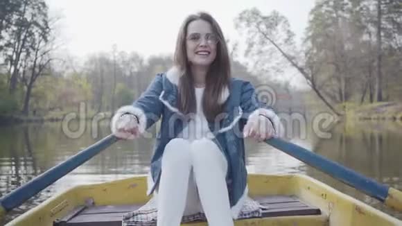 穿着白色裤子穿着牛仔裤夹克戴着墨镜的漂亮年轻魅力女人坐在河上的黄船上看上去视频的预览图