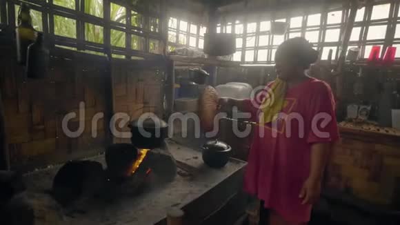 亚洲女人用扇子吹火在竹屋的篝火上煮食物传统的准备晚餐视频的预览图