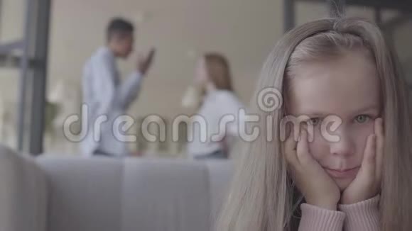 特写小白脸悲伤的女孩坐在沙发上背景是非洲父亲和白种人母亲的剪影视频的预览图