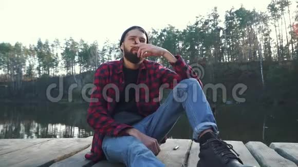 大胡子的人坐在神奇的湖附近抽雪茄视频的预览图