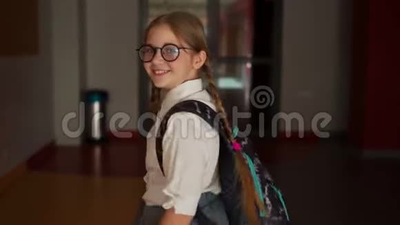 戴眼镜的小女孩带着书包在学校走廊的背景上回到学校视频的预览图