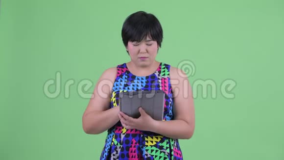 快乐年轻体重超重的亚洲女性使用数码平板电脑思考视频的预览图