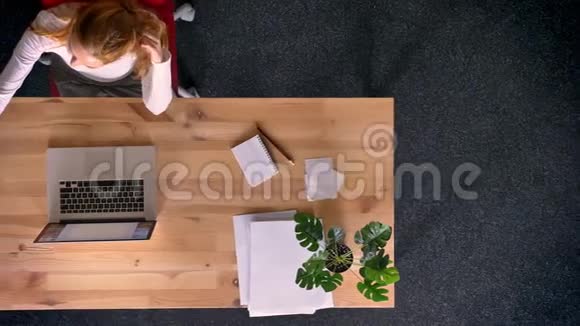 多莉拍摄从上往下看红头发的女人在办公室里用智能手机制作自拍照片视频的预览图