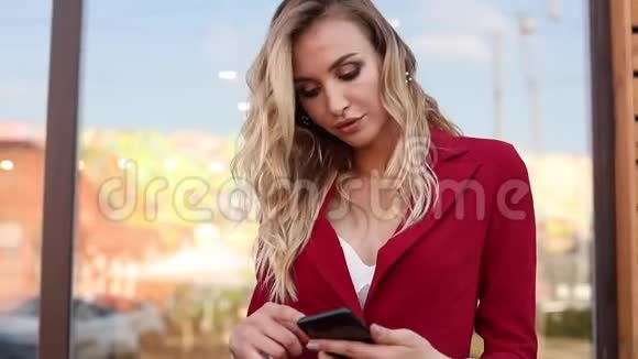 时尚的金发碧眼穿着红色智能套装使用手机和短信视频的预览图