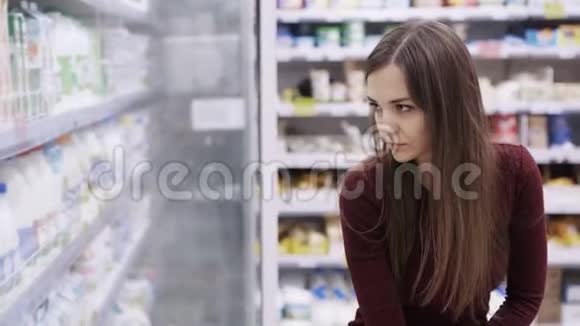 在购物中心食品杂货店的冰箱里挑选奶制品的女人视频的预览图