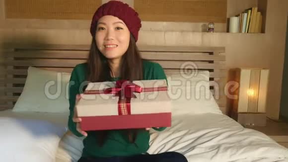 戴着冬帽坐在床上手捧圣诞礼物兴奋地收到圣诞礼品盒的亚洲美女视频的预览图