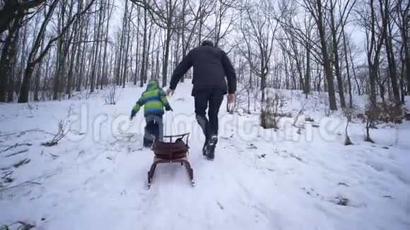 父母支持父亲帮助儿子在冬天用雪橇爬雪山视频的预览图