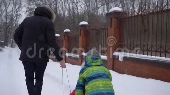 在冬天的周末下雪的时候爸爸在街上橇着他的孩子们视频的预览图