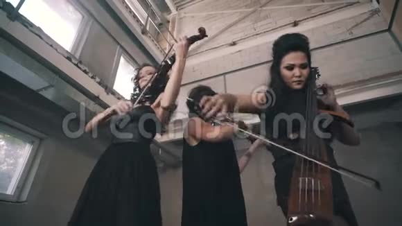 三个穿黑色衣服的小提琴手在一个未完成的房间里演奏视频的预览图
