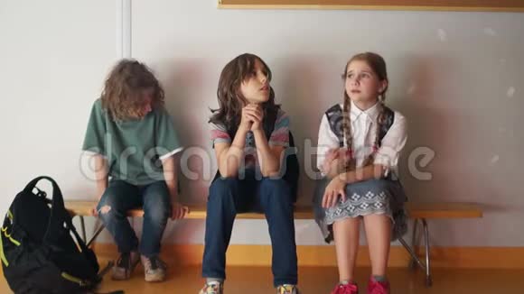 学校里的三个青少年坐在长凳上感到无聊一位面目全非的成人教师在学校里跑来跑去向学生们问好视频的预览图