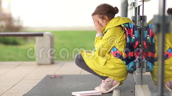 孤独的女孩为侮辱而哭泣坐在学校的门口拿起眼镜和教程离开灯泡视频的预览图