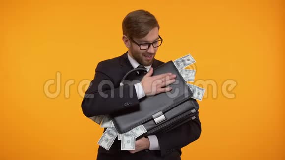 商人抱着装满钱的公文包被孤立在黄色背景上视频的预览图
