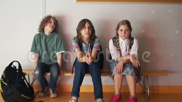 三名学童坐在学校走廊的长凳上等待上课开始回到学校视频的预览图