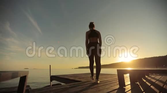 运动女孩在日落时分站在河边的码头上以树的姿势练习瑜伽视频的预览图