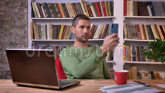 在笔记本电脑前有一个视频电话的商人在椅子上转过身书架在后面视频的预览图