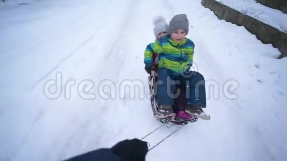 快乐的孩子在冬天雪橇手快带着雪橇和男孩和女孩在雪道上视频的预览图