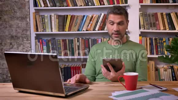 商人坐在笔记本电脑前在平板电脑上交谈背景书架视频的预览图
