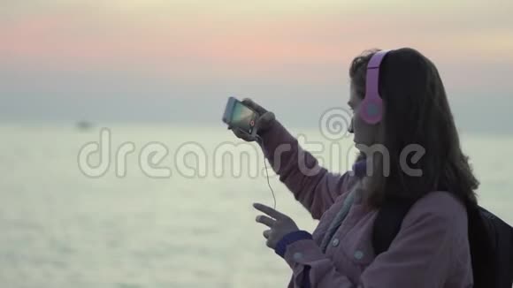 一个女孩正在用她的智能手机拍摄海上日落视频的预览图