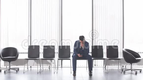 孤独时尚的男人坐在椅子上用电话视频的预览图