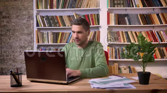 在笔记本电脑上工作的上班族为取得成功而感到高兴背景书架视频的预览图