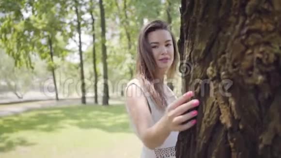 一位年轻貌美的少女长着一头深色长发身穿一件白色的夏装站在一棵树视频的预览图