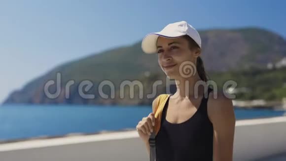 外景肖像美丽时尚性感运动女性穿着黑色泳衣和白色帽子漫步海湾海边视频的预览图