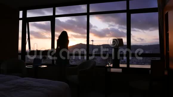 女人望窗外欣赏落日的城市风景视频的预览图