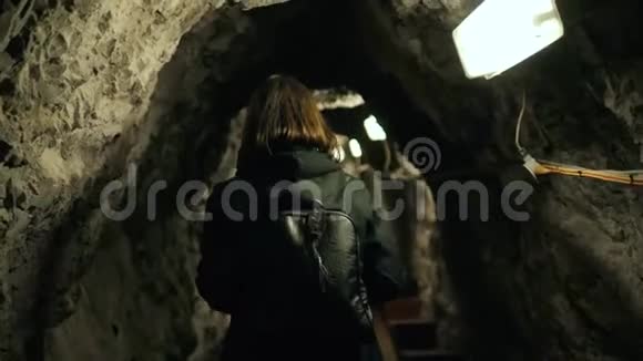 黑暗洞穴中的女人带着背包游客跟随后景石墙之间的编剧女孩视频的预览图