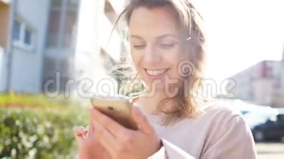 一个女孩带着智能手机在带着智能手机在一条城市街道对面的开花树阳光强烈的布景视频的预览图