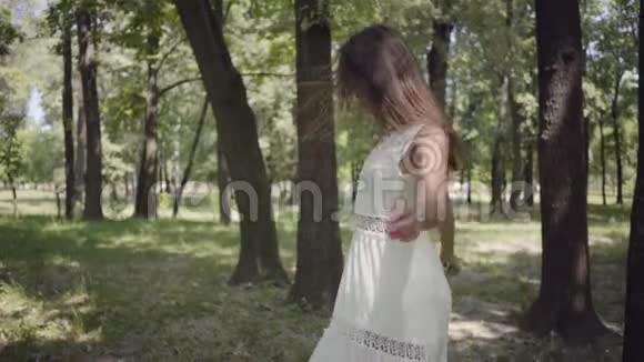 可爱的年轻女孩穿着白色的长夏礼服在公园里旋转一个漂亮女人在户外休闲慢慢视频的预览图