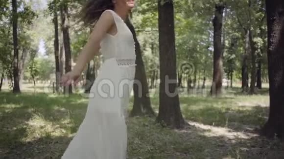 可爱的年轻女孩穿着白色的长夏礼服在公园里旋转一个漂亮女人在户外休闲慢动作视频的预览图
