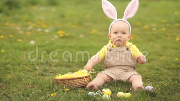 可爱的有趣的小男孩带着兔子耳朵在绿草上玩复活节彩蛋孩子开心地笑着复活节视频的预览图