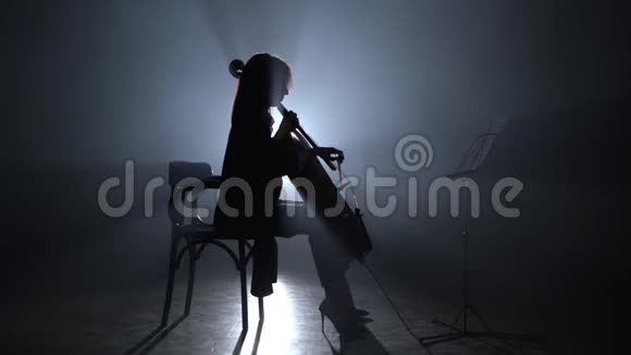 女孩晚上在烟雾弥漫的房间里鞠躬大提琴剪影黑烟背景视频的预览图