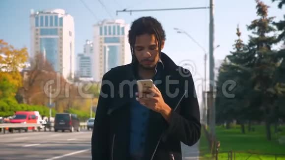 年轻的非裔美国人的肖像带着可怕的人看着智能手机紧张地看着马路视频的预览图
