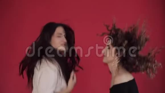 两个快乐的朋友在演播室的红色背景下跳舞和唱歌视频的预览图