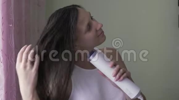 那个女孩用吹风机吹干头发一个没有化妆的年轻女孩用吹风机擦干头发早上的造型视频的预览图