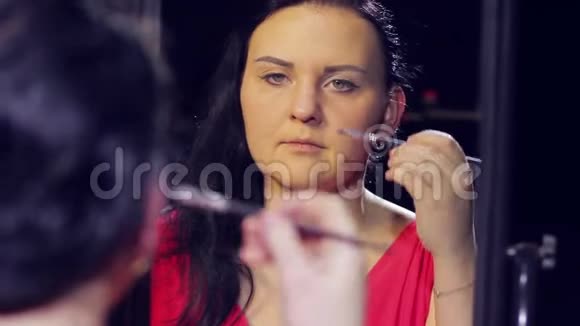 镜子前的一个年轻女人在她的眼睛上化妆视频的预览图