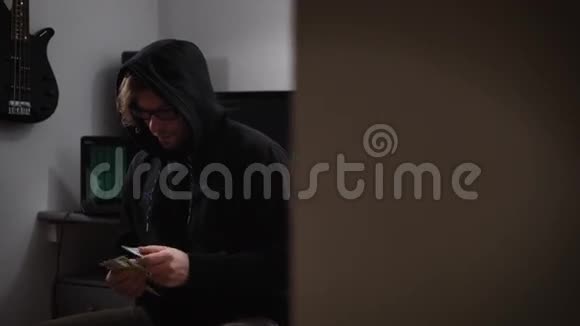 一个电脑室的黑客一个穿着夹克衫戴着兜帽戴着眼镜手里拿着钱坐在椅子上的人一个男人视频的预览图