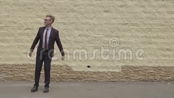 英俊而快乐的商人在城市混凝土墙前的一条街上精力充沛地跳舞戴着微笑的男人视频的预览图
