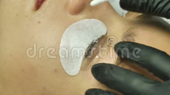 这位美容师用一层透明的眼睑罩上女性的眼睛在睫毛上抹上平滑的白色奶油视频的预览图