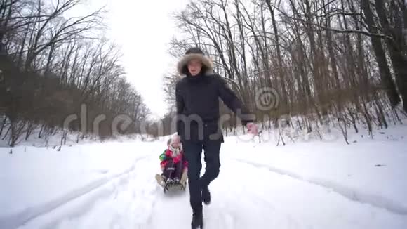 周末年轻的父母带着雪橇和快乐的孩子在雪林视频的预览图
