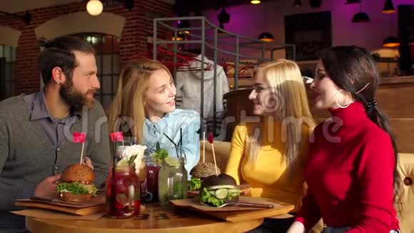 四个朋友在一家明亮的阳光咖啡馆里吃汉堡包和喝柠檬水视频的预览图