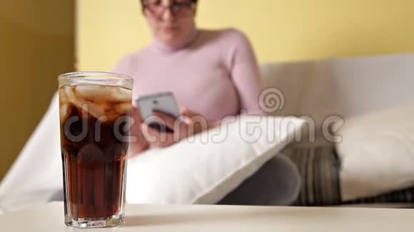 戴眼镜的女人呆在家里用电话和可口可乐一起喝威士忌视频的预览图