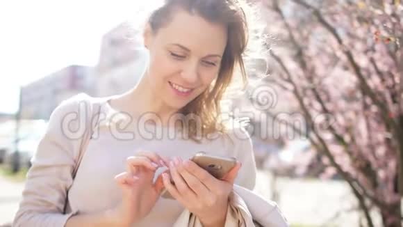 成熟的女人手里拿着智能手机微笑着玉兰盛开在城市街道上春天的肖像视频的预览图