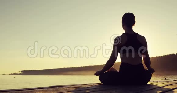 日落时分坐在河边的码头上的莲花波斯正在冥想视频的预览图
